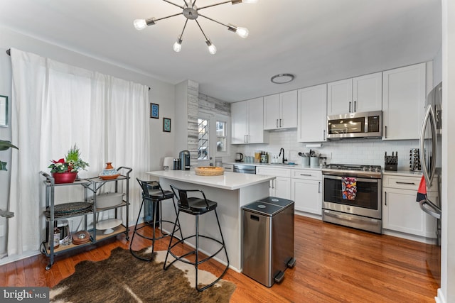 kitchen featuring hardwood / wood-style floors, a kitchen bar, sink, white cabinetry, and appliances with stainless steel finishes