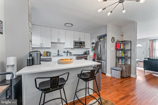 kitchen with backsplash, white cabinetry, hardwood / wood-style flooring, appliances with stainless steel finishes, and a kitchen breakfast bar