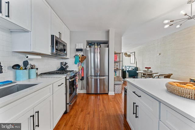 kitchen featuring backsplash, a notable chandelier, white cabinetry, light wood-type flooring, and appliances with stainless steel finishes