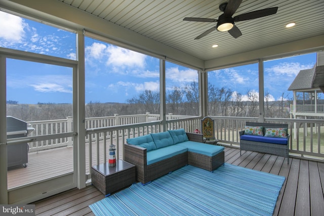 sunroom / solarium with a wooded view and a ceiling fan