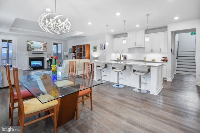 dining area featuring dark wood finished floors, recessed lighting, a raised ceiling, a glass covered fireplace, and stairs