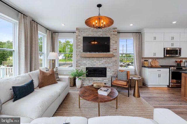 living room featuring a notable chandelier, a brick fireplace, and light hardwood / wood-style flooring