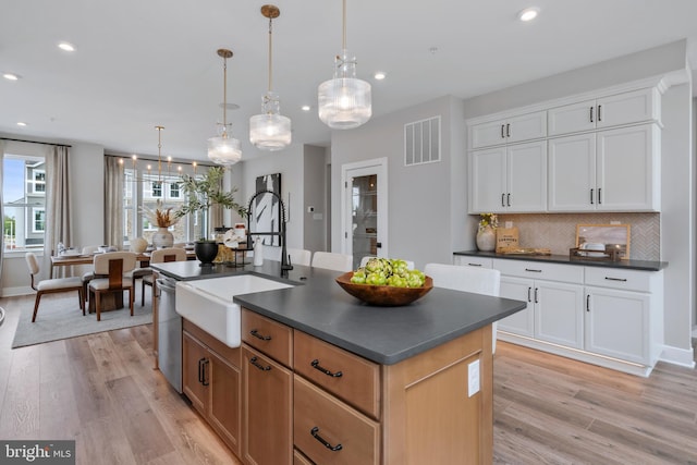 kitchen featuring pendant lighting, sink, tasteful backsplash, an island with sink, and white cabinets