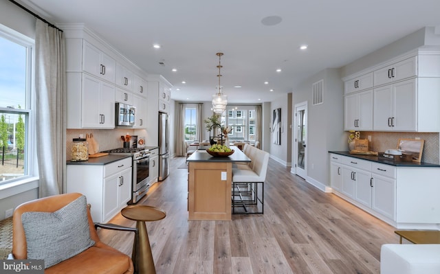 kitchen with white cabinetry, hanging light fixtures, light hardwood / wood-style flooring, an island with sink, and stainless steel appliances