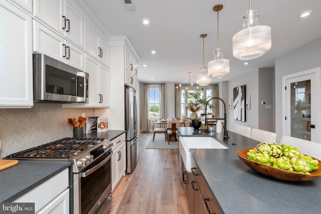 kitchen with decorative light fixtures, backsplash, white cabinets, stainless steel appliances, and light wood-type flooring