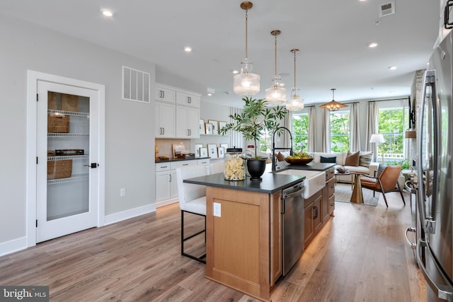 kitchen featuring sink, hanging light fixtures, appliances with stainless steel finishes, an island with sink, and white cabinets