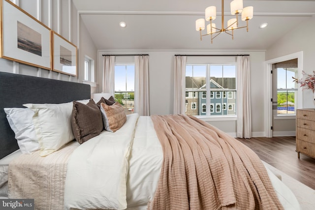 bedroom featuring multiple windows, wood-type flooring, lofted ceiling, and an inviting chandelier