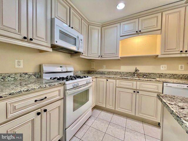 kitchen featuring light stone countertops, white appliances, sink, cream cabinets, and light tile patterned floors