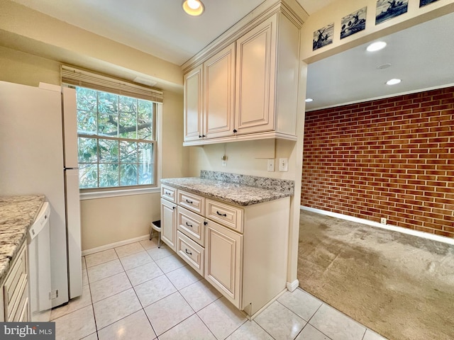 kitchen with light carpet, cream cabinetry, light stone countertops, and brick wall