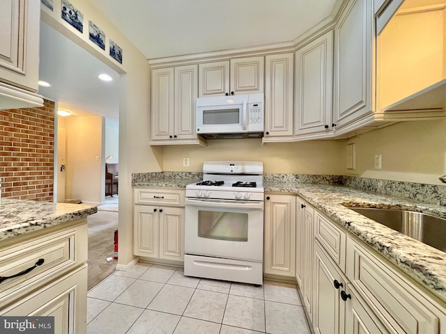 kitchen featuring light tile patterned floors, white appliances, light stone countertops, cream cabinets, and sink