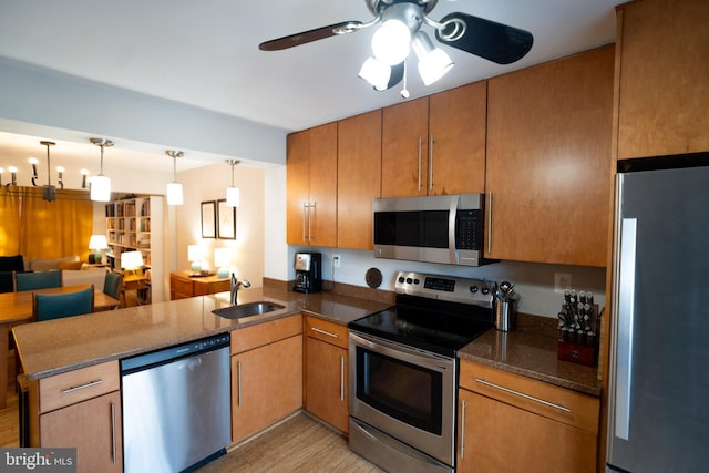 kitchen featuring appliances with stainless steel finishes, sink, hanging light fixtures, kitchen peninsula, and light wood-type flooring