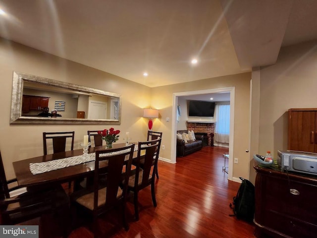 dining space with a baseboard heating unit, dark hardwood / wood-style floors, and a brick fireplace