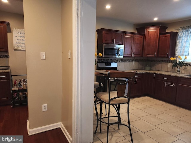 kitchen featuring light stone countertops, stove, tasteful backsplash, dark brown cabinets, and light tile patterned floors