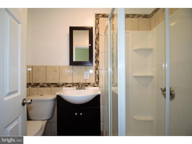 bathroom featuring vanity, a shower with shower door, tile walls, and toilet