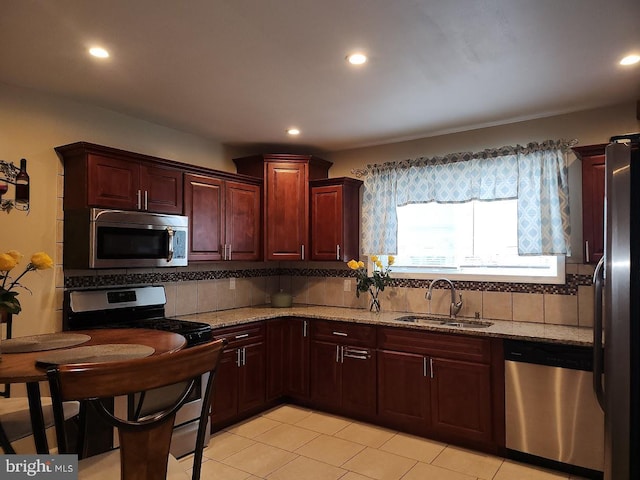 kitchen with light stone countertops, appliances with stainless steel finishes, backsplash, sink, and light tile patterned floors