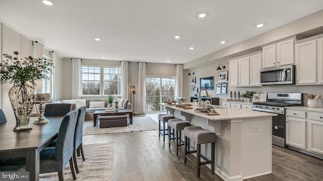 kitchen featuring a center island with sink, white cabinets, sink, appliances with stainless steel finishes, and a breakfast bar area