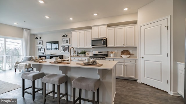 kitchen featuring white cabinets, a breakfast bar, stainless steel appliances, and an island with sink