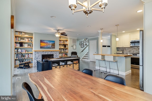 dining space with ceiling fan with notable chandelier, a fireplace, and light hardwood / wood-style floors