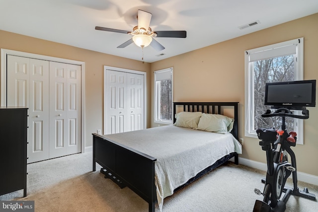 bedroom featuring multiple closets, light carpet, and ceiling fan