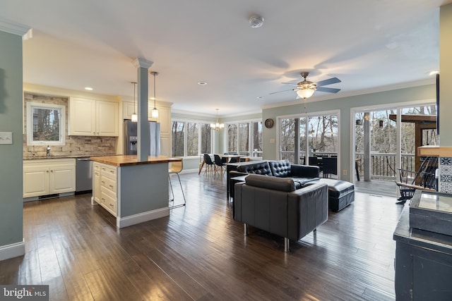 living room with ornate columns, crown molding, dark wood-type flooring, and ceiling fan with notable chandelier