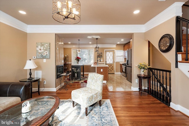 living room featuring sink, light hardwood / wood-style flooring, ornamental molding, and a chandelier