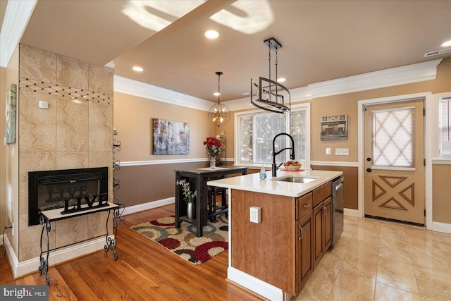 kitchen with pendant lighting, sink, a tiled fireplace, a kitchen island with sink, and stainless steel dishwasher