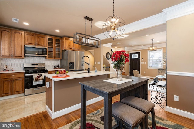 kitchen with crown molding, pendant lighting, stainless steel appliances, a kitchen island with sink, and decorative backsplash