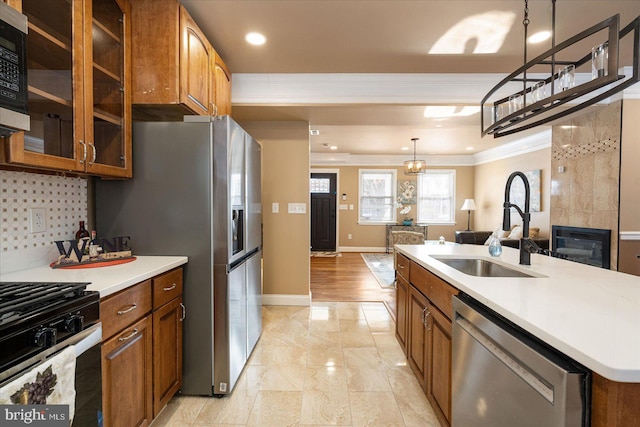 kitchen with sink, a center island with sink, ornamental molding, appliances with stainless steel finishes, and pendant lighting