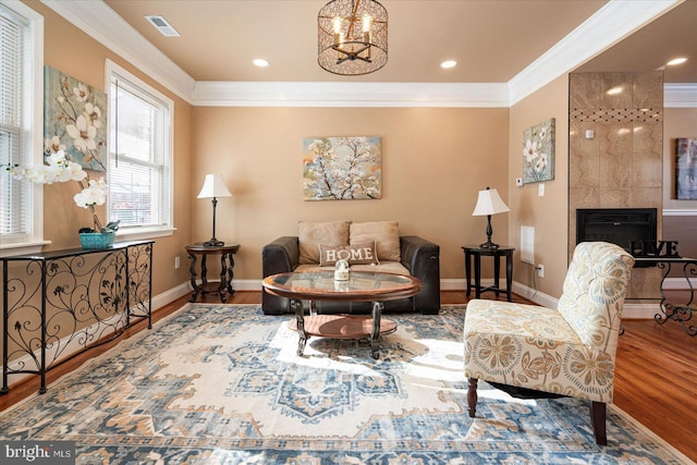 living area with a tiled fireplace, crown molding, wood-type flooring, and an inviting chandelier