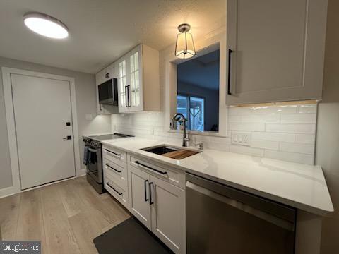 kitchen with white cabinets, dishwasher, sink, range with electric cooktop, and light wood-type flooring