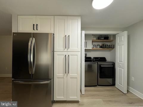 kitchen with light wood-type flooring, white cabinetry, stainless steel fridge, and washer and dryer