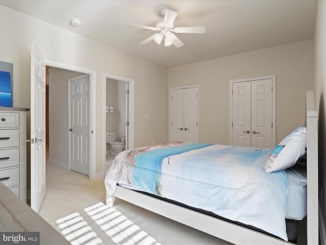 bedroom featuring ceiling fan, light colored carpet, ensuite bath, and multiple closets