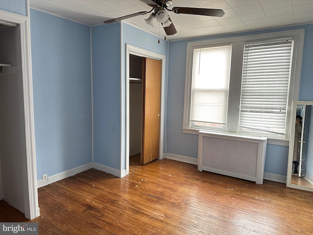 unfurnished bedroom with radiator heating unit, a closet, ceiling fan, and hardwood / wood-style floors