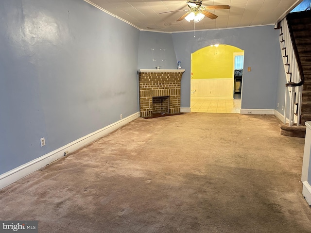 unfurnished living room with carpet flooring, a brick fireplace, ceiling fan, and crown molding