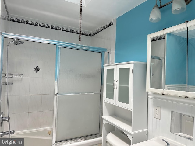 bathroom featuring toilet and bath / shower combo with glass door