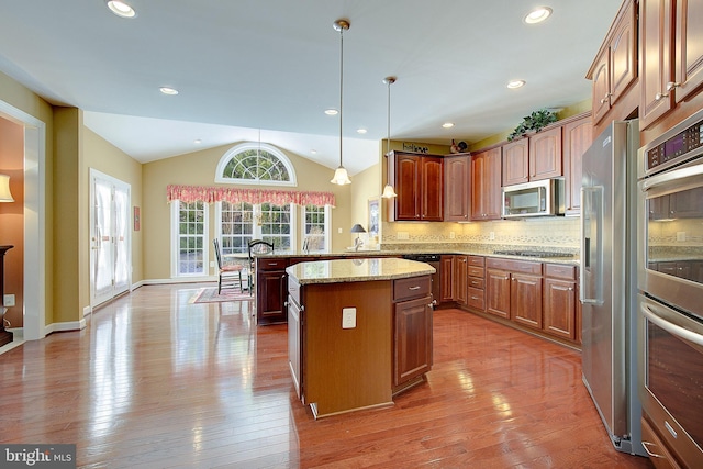 kitchen featuring vaulted ceiling, appliances with stainless steel finishes, decorative light fixtures, kitchen peninsula, and light stone countertops