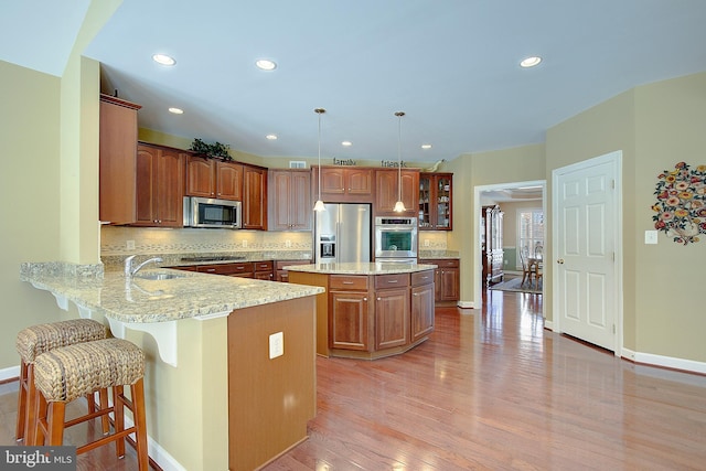 kitchen with pendant lighting, sink, stainless steel appliances, a center island, and kitchen peninsula