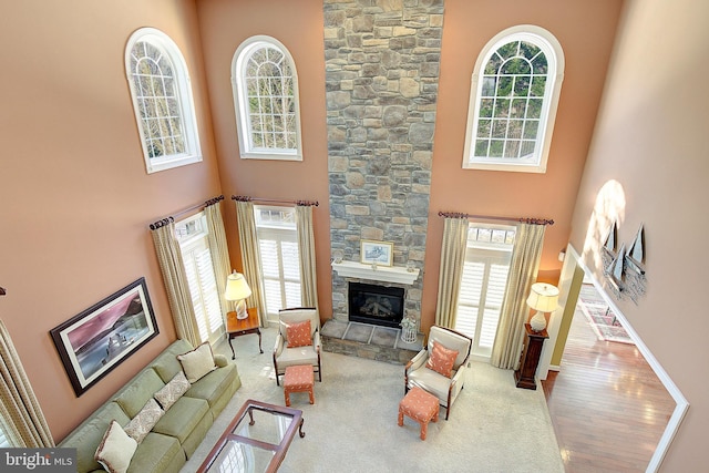 carpeted living room featuring a towering ceiling, a stone fireplace, and a wealth of natural light