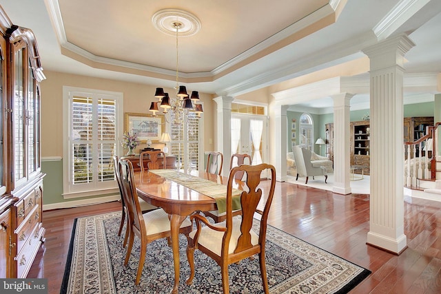 dining space with dark hardwood / wood-style floors, ornamental molding, a tray ceiling, and decorative columns