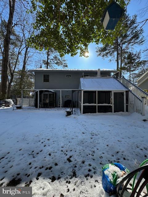 snow covered rear of property with a sunroom