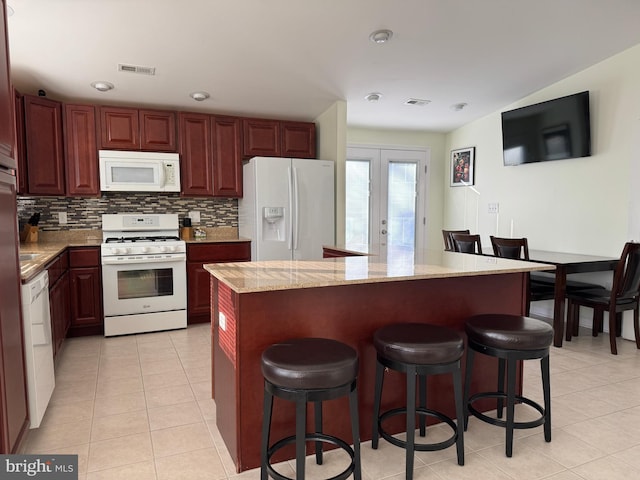 kitchen featuring light tile patterned flooring, french doors, light stone counters, a kitchen island, and white appliances