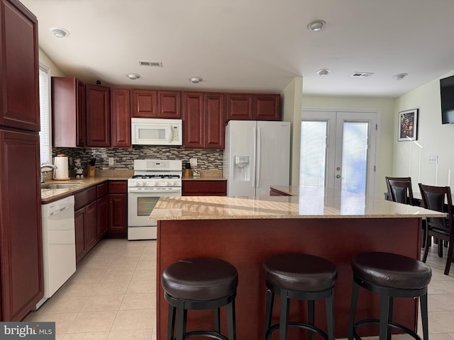 kitchen with sink, white appliances, a kitchen island, light tile patterned flooring, and french doors