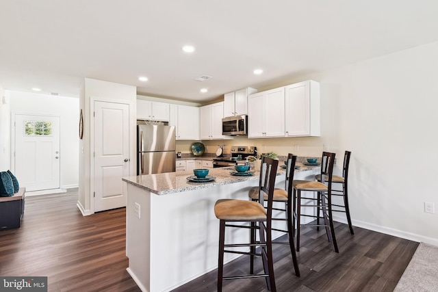 kitchen with white cabinets, appliances with stainless steel finishes, a kitchen breakfast bar, and dark hardwood / wood-style floors