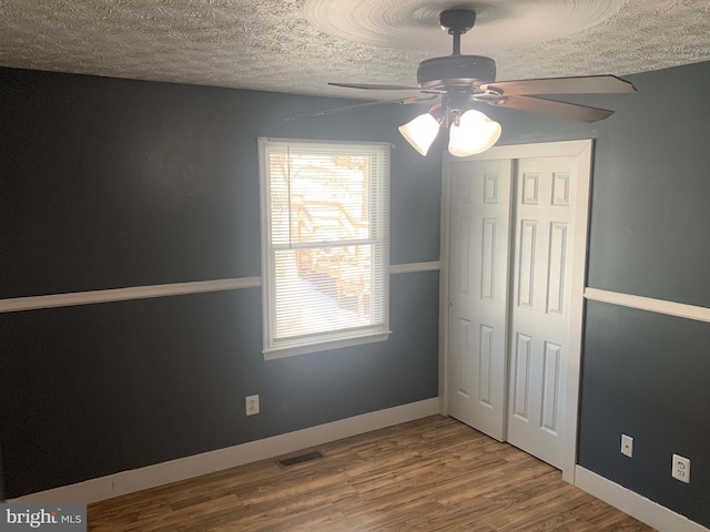 unfurnished bedroom featuring ceiling fan, a closet, a textured ceiling, and hardwood / wood-style flooring