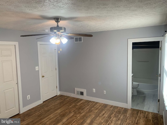 unfurnished bedroom with a textured ceiling, connected bathroom, ceiling fan, and dark hardwood / wood-style floors