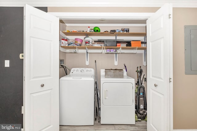 clothes washing area featuring electric panel, washer and clothes dryer, and light hardwood / wood-style flooring