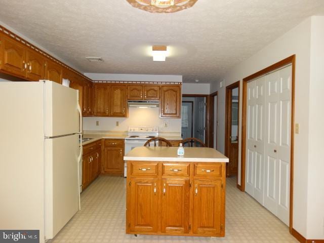 kitchen featuring a textured ceiling, a center island with sink, and white appliances