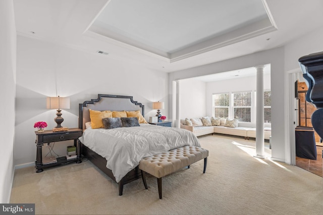 bedroom featuring decorative columns, a tray ceiling, and light carpet