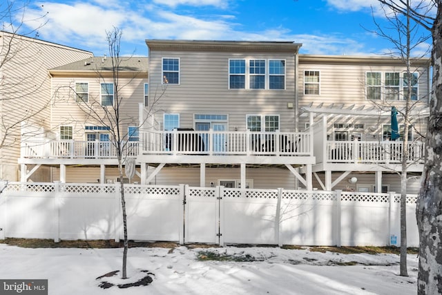 snow covered back of property with a wooden deck and a pergola