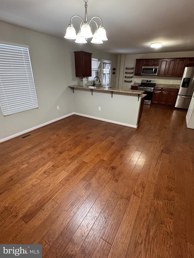 kitchen with a kitchen breakfast bar, a notable chandelier, kitchen peninsula, pendant lighting, and appliances with stainless steel finishes